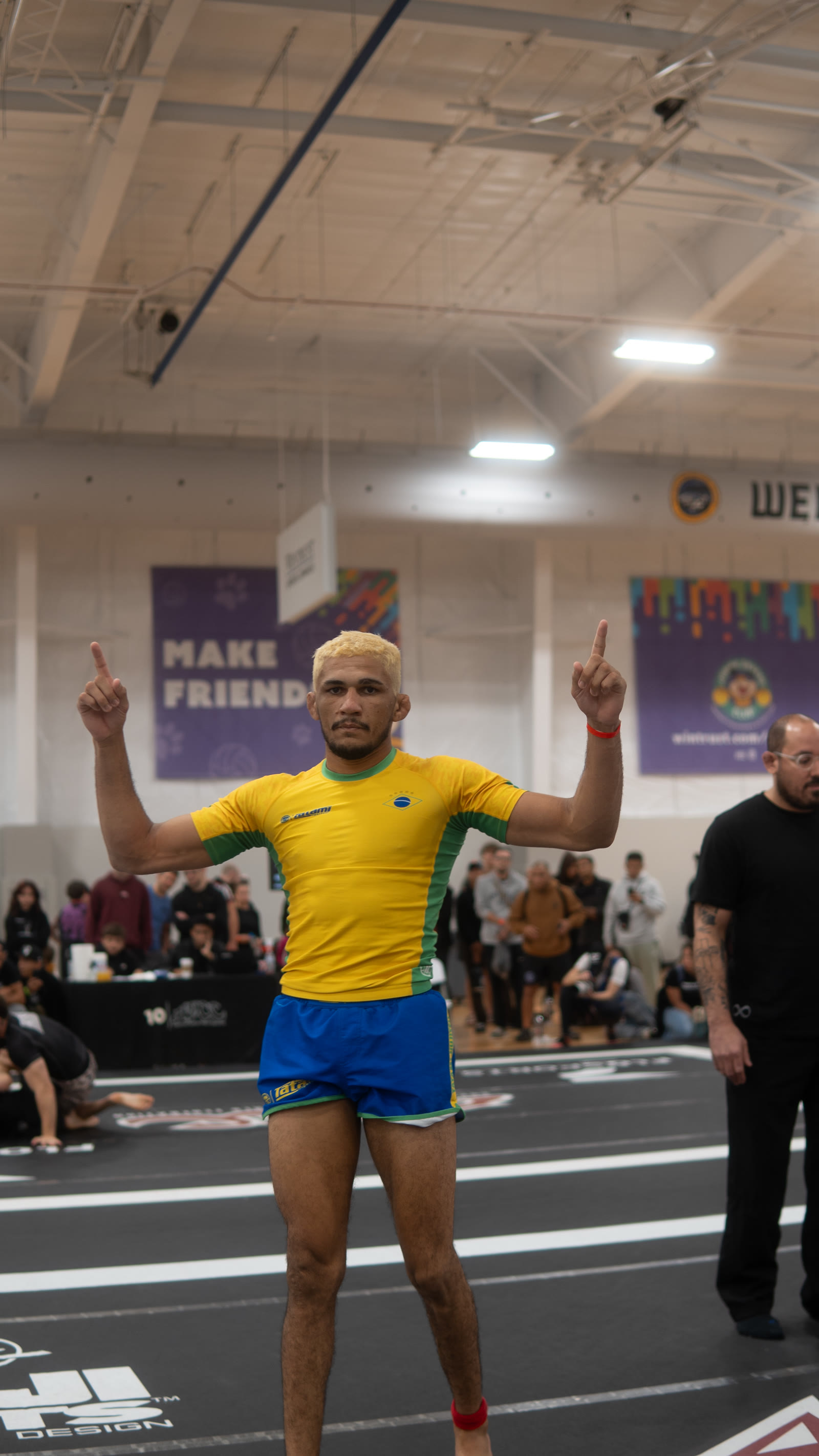 Wellington Andrade on the mat in a yellow and green rashguard, both arms raised.